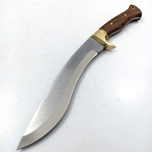 Puede incluir: Un cuchillo curvo de color plateado con un mango de madera. El mango es marr&oacute;n con un acento de lat&oacute;n. El cuchillo est&aacute; sobre un fondo blanco.