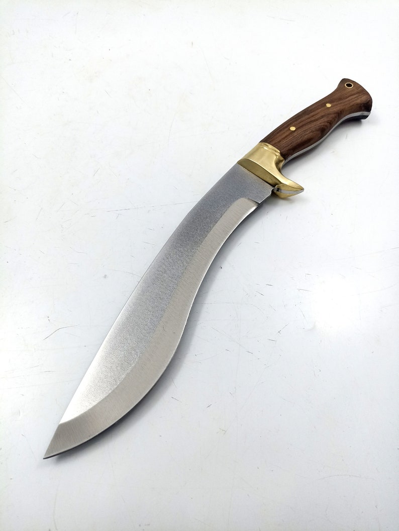 Puede incluir: Un cuchillo curvo de color plateado con un mango de madera. El mango es marr&oacute;n con un acento de lat&oacute;n. El cuchillo est&aacute; sobre un fondo blanco.