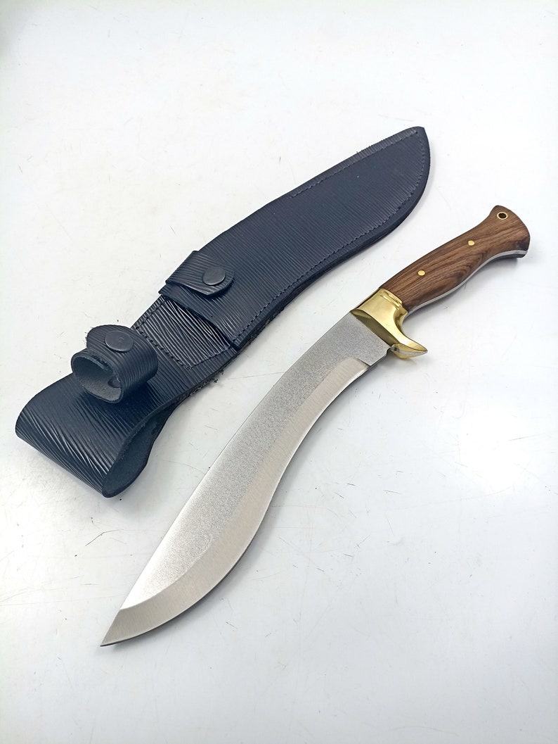 Puede incluir: Un cuchillo plateado y dorado con mango de madera y una funda de cuero negro.