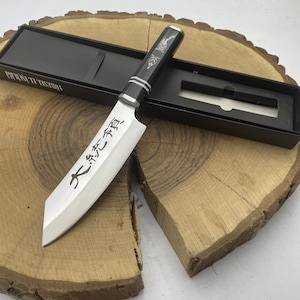 May include: A black and silver kitchen knife with a wooden handle. The blade has Japanese characters inscribed on it. The knife is in a black box with the words "Yoshihiro" printed on it.