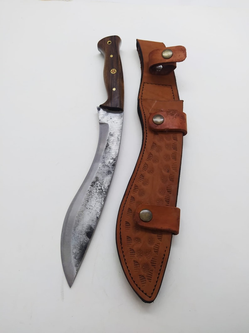 May include: A curved, silver-colored knife with a wooden handle and a brown leather sheath. The sheath has a decorative pattern and a snap closure.