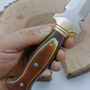 Op de afbeelding: Een jachtmes met een bruin en zwart houten handvat en gouden accenten.