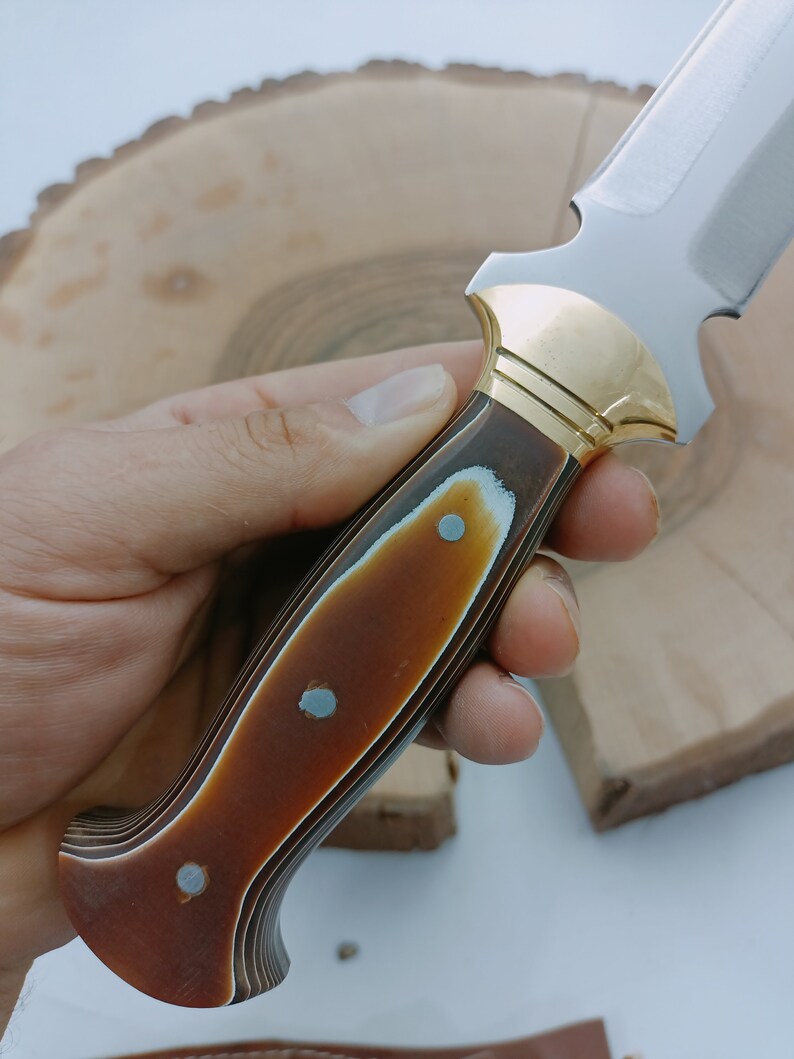Op de afbeelding: Een jachtmes met een bruin en zwart houten handvat en gouden accenten.