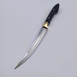 May include: A long, curved, silver knife with a black handle and gold accents. The blade has a slight curve and a sharp point. The handle is made of wood and has a textured surface.
