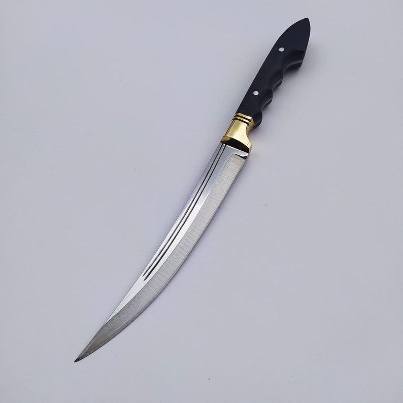 May include: A long, curved, silver knife with a black handle and gold accents. The blade has a slight curve and a sharp point. The handle is made of wood and has a textured surface.