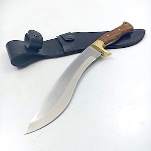 Puede incluir: Un cuchillo curvo plateado con mango de madera y una funda de cuero negro.