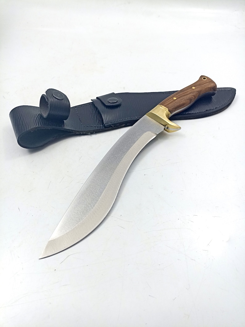 Puede incluir: Un cuchillo curvo plateado con mango de madera y una funda de cuero negro.