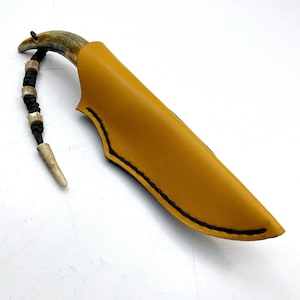 May include: A yellow leather knife sheath with black stitching. The sheath has a curved shape and a pointed tip. A small, decorative antler handle is visible at the top of the sheath.