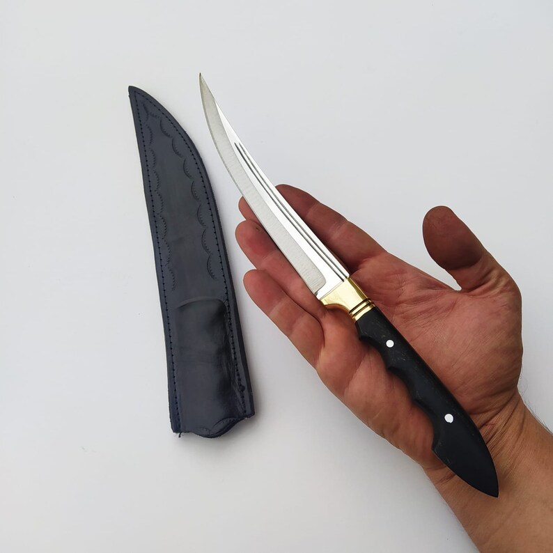 May include: A black-handled knife with a silver blade and a gold accent. The knife is in a black leather sheath.