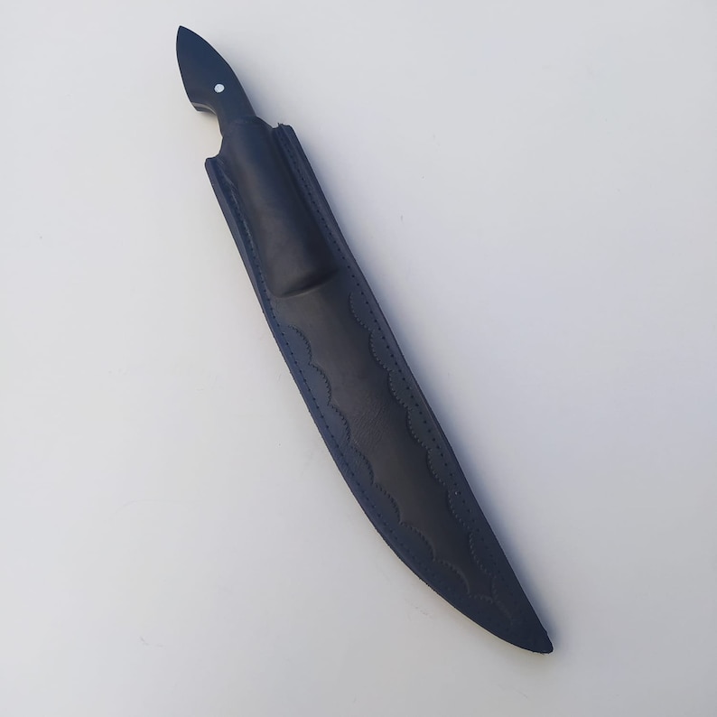 May include: A black leather knife sheath with a decorative wave pattern. The sheath is designed to hold a knife with a black handle.