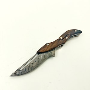 Könnte beinhalten: Ein kleines, klappbares Messer mit einer gemusterten Klinge aus Stahl und einem Griff aus dunklem Holz.