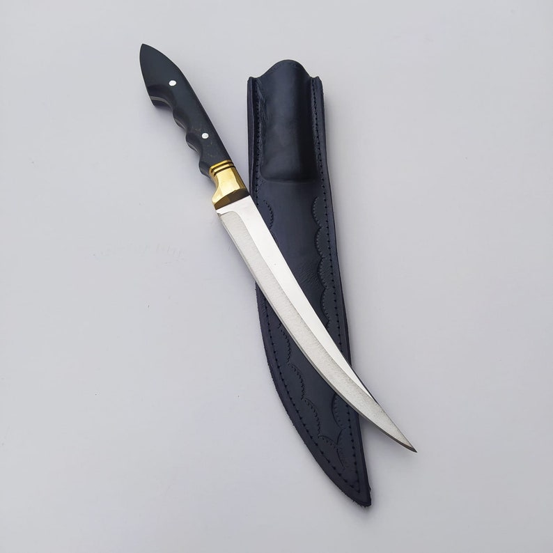 May include: A black-handled knife with a gold accent and a silver blade. The knife is in a black leather sheath.
