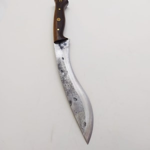 May include: A curved, silver-colored knife with a wooden handle. The handle has a dark brown color and gold accents.