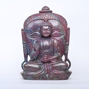 May include: A carved stone statue of a seated Buddha with a serene expression. The statue is made of a deep red and purple stone with intricate details. The Buddha is seated in a meditative pose with hands in the Dhyana mudra.