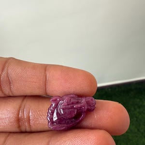 May include: A carved, deep red gemstone in the shape of a horse's head. The gemstone is held between fingers, showcasing the intricate details of the carving and the polished surface. The horse's head is facing right.