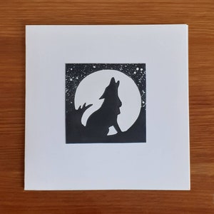 Peut inclure: Une carte noire et blanche avec une silhouette de loup hurlant à la lune. La lune est un cercle blanc avec un contour noir. Le loup fait face au côté gauche de la carte.