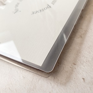 May include: A white planner with a clear plastic cover and a silver ring binding. The planner has the text "It's your power and that is your magic" printed on the cover.