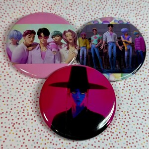 Può includere: Tre bottoni rotondi con immagini colorate. Un bottone è rosa con un gruppo di persone. Un altro bottone ha un gruppo di persone su uno sfondo colorato. Il terzo bottone è rosso con una persona con un cappello nero.