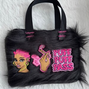 May include: Black faux fur tote bag with pink accents. The bag features three embroidered patches: a cartoon woman with pink hair, a hand holding a lit cigarette, and the words "Puff Puff Pass".