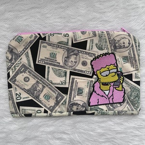 May include: A pink zippered pouch with a cartoon character on the front. The character is yellow with pink hair and is holding a phone to their ear. The pouch is covered in a pattern of US dollar bills.