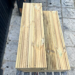 May include: Two wooden planks with grooved surfaces, stacked on top of each other. The planks are light brown with a slightly weathered appearance.
