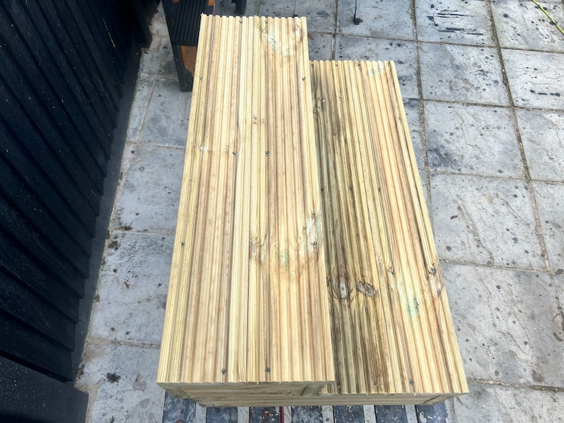 May include: Two wooden planks with grooved surfaces, stacked on top of each other. The planks are light brown with a slightly weathered appearance.