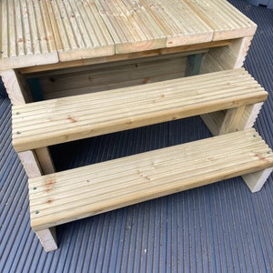 May include: Wooden steps with three tiers, made of light brown wood with a grooved surface. The steps are designed for entering a hot tub or pool.