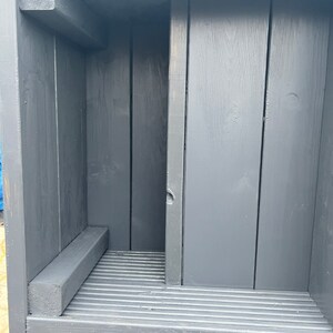May include: A dark gray wooden shelf unit with a slatted shelf and a small ledge. The shelf unit is made of unfinished wood and has a rustic look.