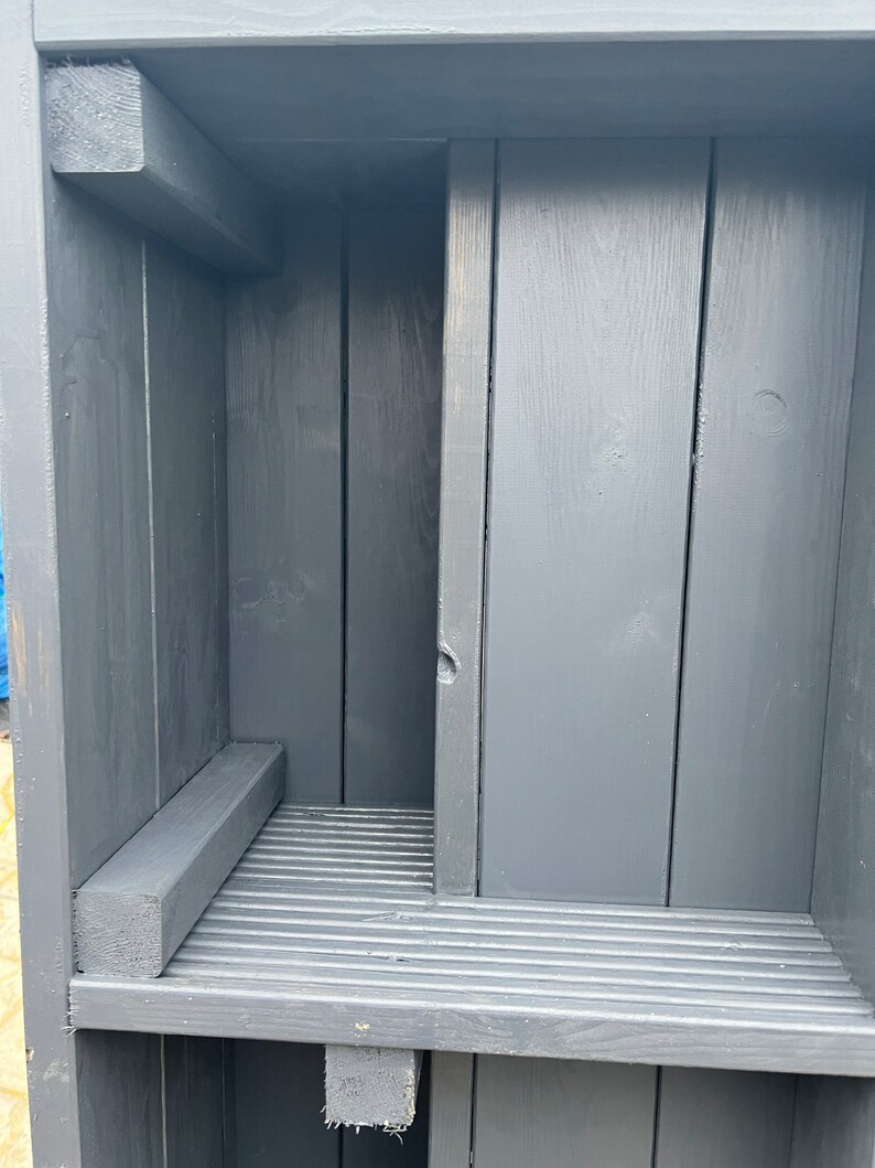 May include: A dark gray wooden shelf unit with a slatted shelf and a small ledge. The shelf unit is made of unfinished wood and has a rustic look.
