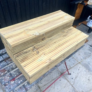 May include: Two wooden steps made of stacked planks, the top step is wider than the bottom step. The steps are sitting on a black metal table with a gray painted surface.