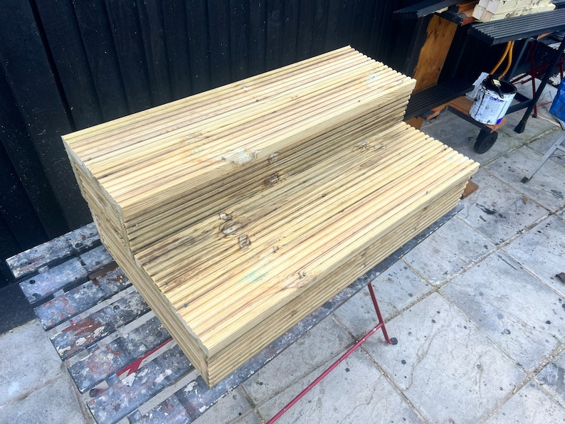 May include: Two wooden steps made of stacked planks, the top step is wider than the bottom step. The steps are sitting on a black metal table with a gray painted surface.