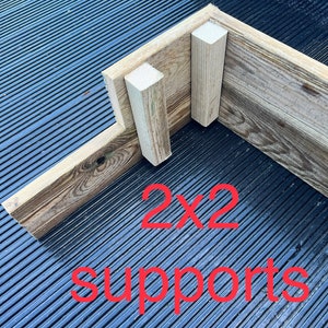 May include: Close-up of a wooden corner joint with two 2x2 supports. The text "2x2 supports" is written in red below the joint.