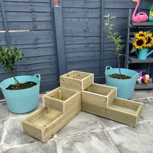 May include: A wooden tiered planter with four rectangular sections. The planter is made of light brown wood and has a natural finish. The planter is sitting on a grey patio.