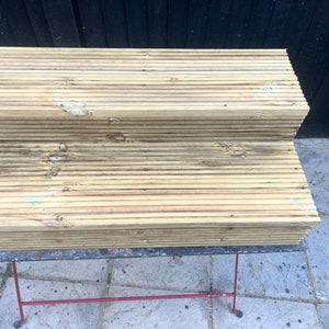 May include: Stacked wooden planks, likely for a deck or patio project, with a weathered, natural finish.