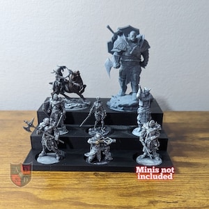 May include: A black plastic tiered display stand for miniature figures. The stand has three tiers and can hold up to eight figures. The stand is empty, but the image shows examples of figures that could be displayed on it. The text "minis not included" is printed on the bottom right corner of the image.