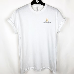 May include: White t-shirt with a gold harp logo and the text "DRUM N BASS" printed on the front.