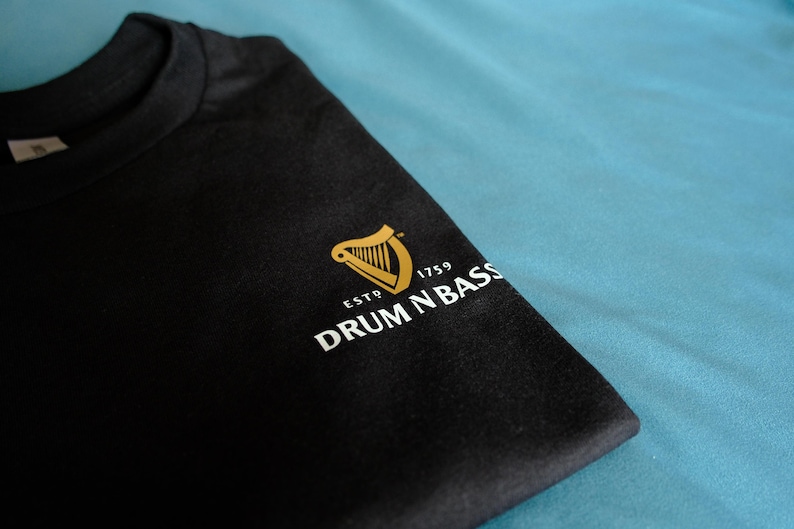 May include: Black t-shirt with a gold harp logo and the text "ESTD 1759 DRUM N BASS" in white.