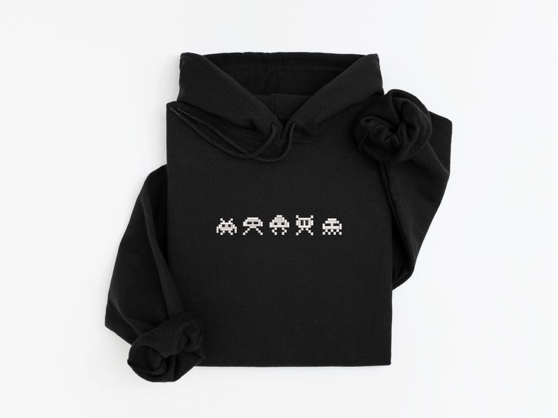 May include: Black hooded sweatshirt with a white pixelated video game graphic across the chest. The graphic features four retro space invader-style characters. The sweatshirt has a drawstring hood and long sleeves.