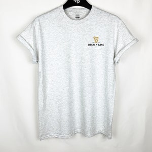 May include: A gray t-shirt with a gold harp logo and the text "Drum N Bass" printed on the front.