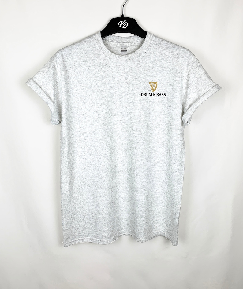 May include: A gray t-shirt with a gold harp logo and the text "Drum N Bass" printed on the front.
