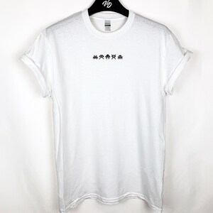 May include: White t-shirt with rolled-up sleeves, featuring a small black pixelated alien design across the chest. The shirt is hanging on a black hanger. The design is reminiscent of classic arcade games.