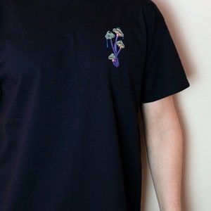 Peut inclure: Un t-shirt noir avec un motif brod&eacute; de champignons violets sur la poitrine gauche.