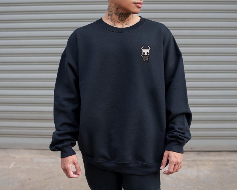 May include: Black crewneck sweatshirt with a small embroidered design on the chest. The design features a white and brown character. The sweatshirt is made of a soft material and has long sleeves.