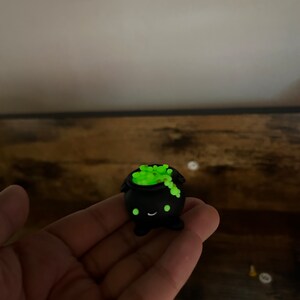 Peut inclure: Petite figurine de chaudron noir avec un visage souriant et un contenu vert vif et bouillonnant. Le chaudron a une forme arrondie et est probablement fait d'un mat&eacute;riau durable. Le contenu vert semble briller. D&eacute;coration fantaisiste sur le th&egrave;me d'Halloween.