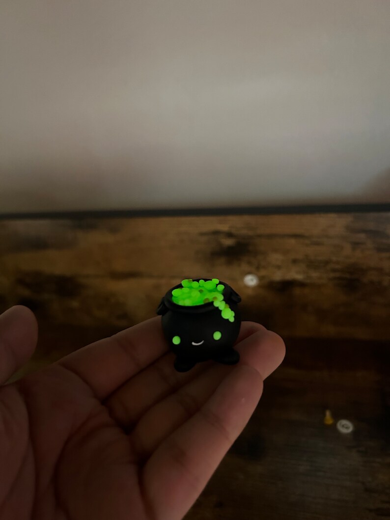 Peut inclure: Petite figurine de chaudron noir avec un visage souriant et un contenu vert vif et bouillonnant. Le chaudron a une forme arrondie et est probablement fait d'un mat&eacute;riau durable. Le contenu vert semble briller. D&eacute;coration fantaisiste sur le th&egrave;me d'Halloween.