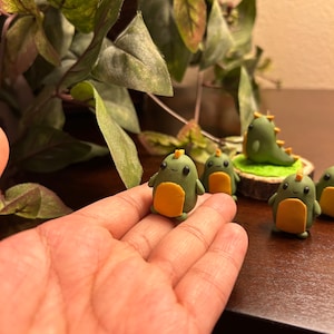 May include: Five small green and yellow dinosaur figurines with smiling faces. The dinosaurs are made of polymer clay and are about 2 inches tall.