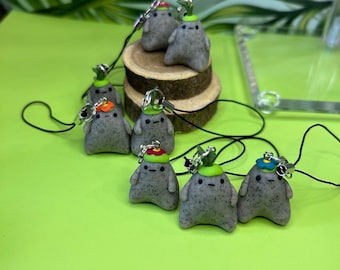 May include: Eight grey, round, handmade charms with different coloured flower accents. Each charm has a small green leaf and is attached to a black string.