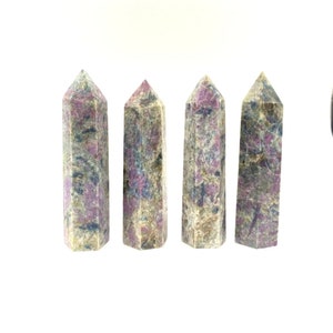 May include: Four grey, purple and white gemstone points, also known as ruby in zoisite, arranged in a row on a white background.