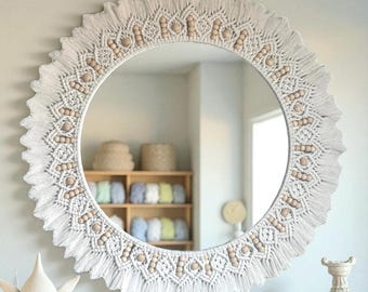 May include: Round white macrame mirror with a decorative fringe and wooden beads. The mirror has a circular shape and is surrounded by a detailed macrame design. The mirror reflects a room with shelves and decorative items.