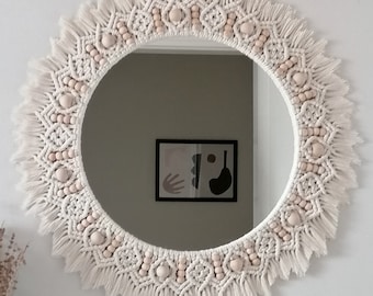 May include: A round macrame mirror with a white cotton cord and wooden beads. The mirror has a fringe border.